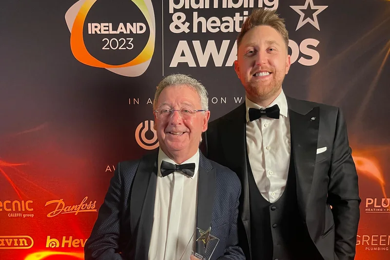 Two of the team holding the trophy in front of the Plumbing & Heating Awards Ireland 2023 backdrop