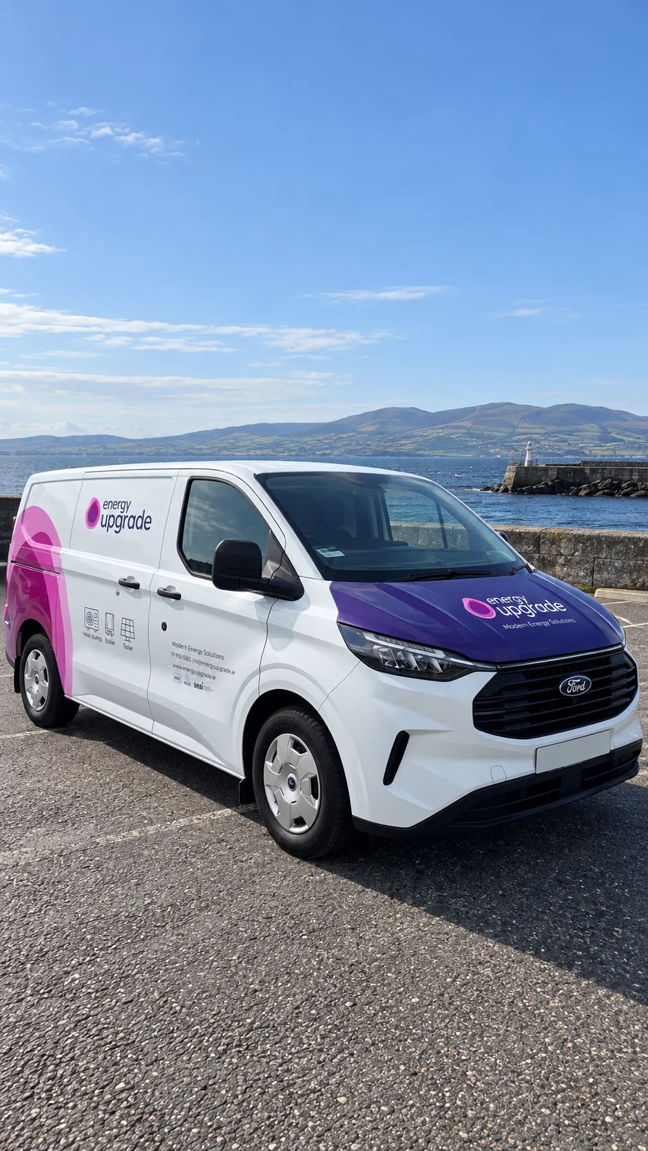 An Energy Upgrade van parked on the coast road with mountains across the bay